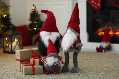 Photo of Funny Christmas gnomes with gift boxes on floor near fireplace indoors