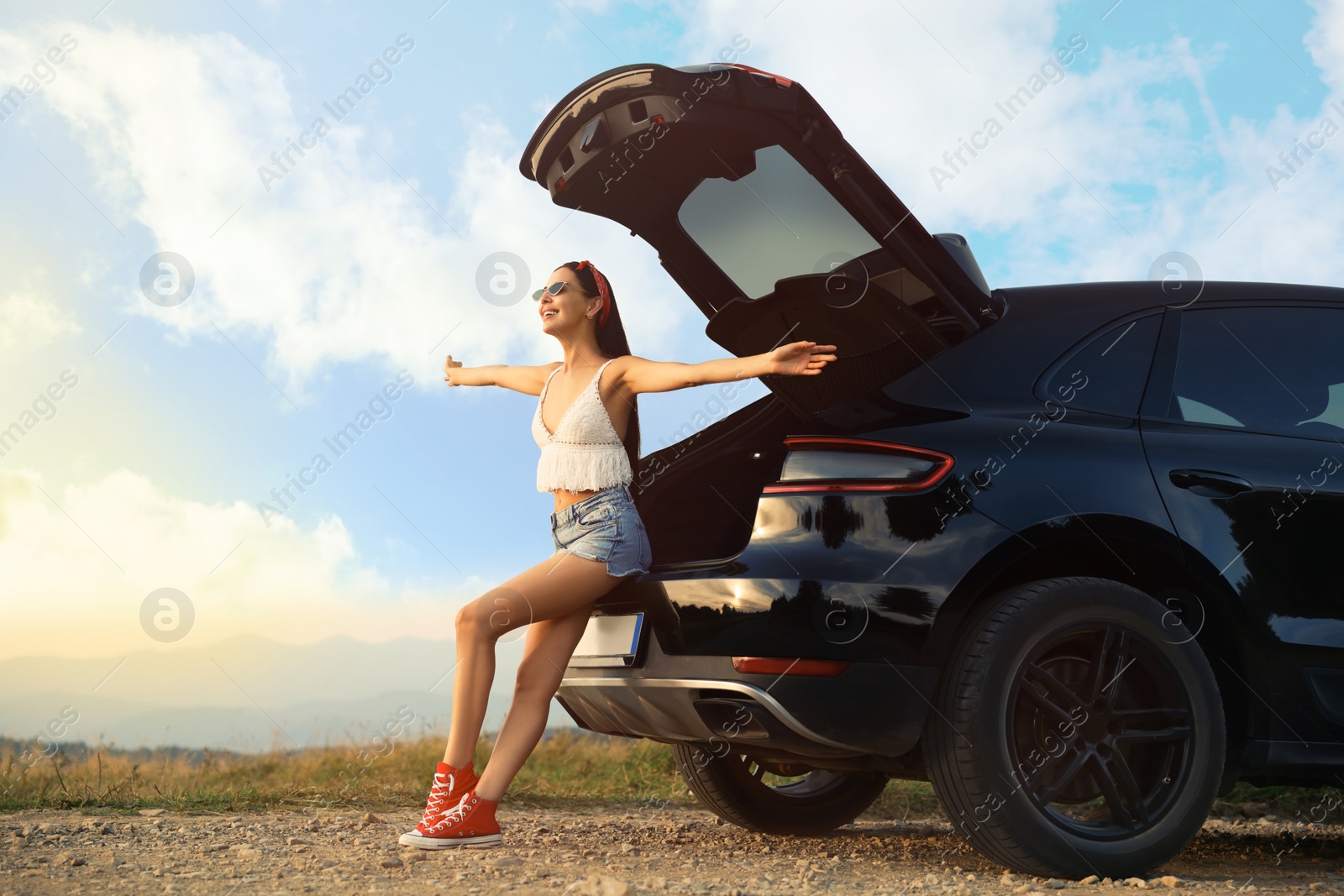 Photo of Happy woman sitting in trunk of modern car on roadside outdoors