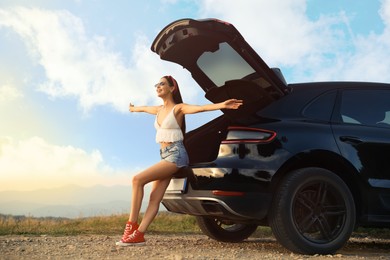 Photo of Happy woman sitting in trunk of modern car on roadside outdoors