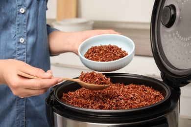 Photo of Woman putting delicious brown rice into bowl from multi cooker, closeup