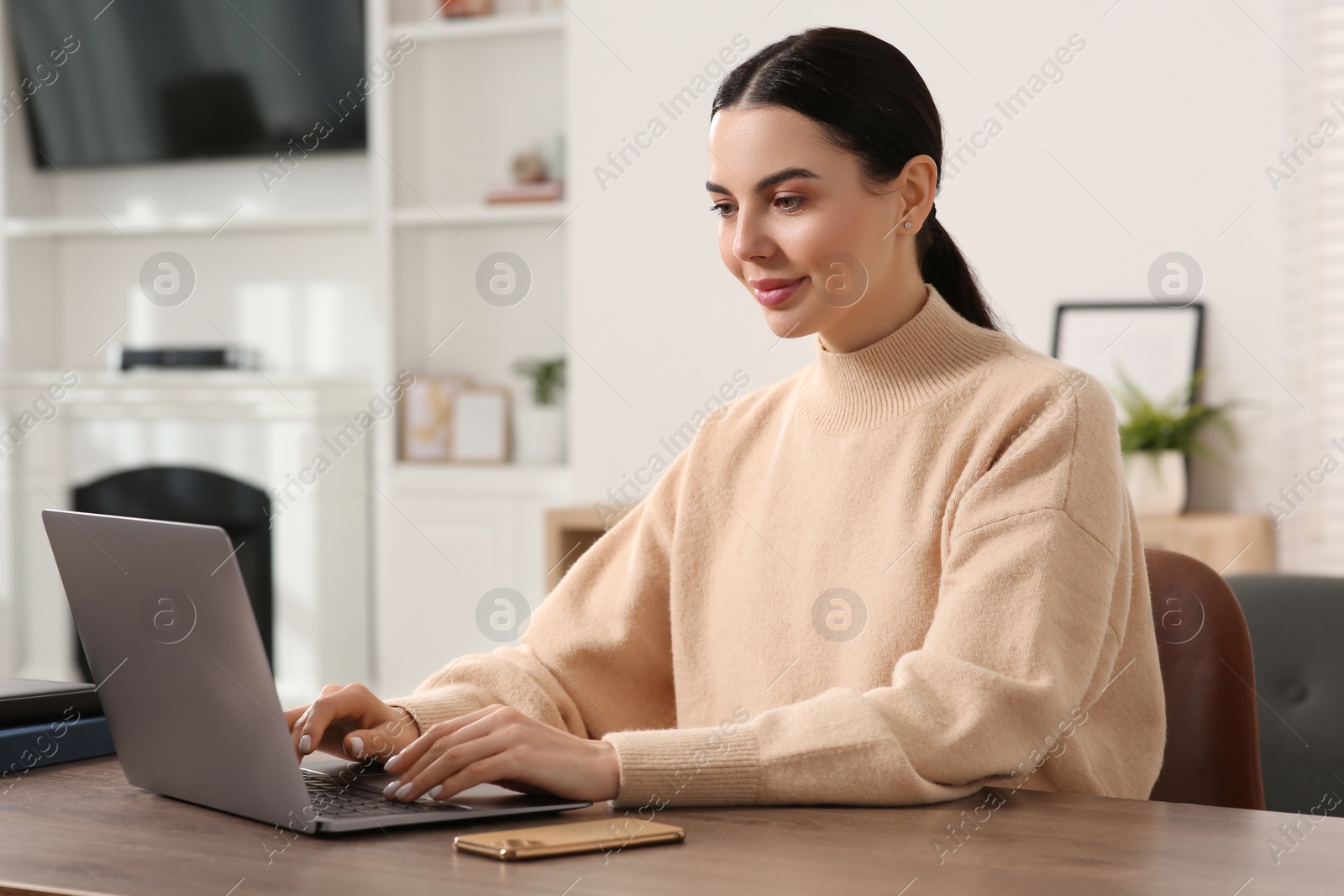 Photo of Woman working with laptop at wooden desk in room