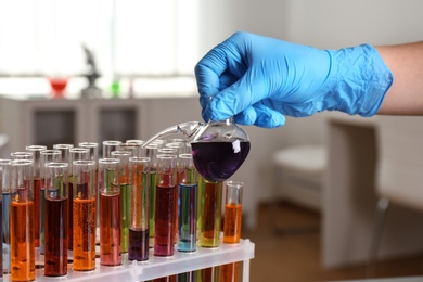 Photo of Scientist pouring liquid from retort flask into test tube at laboratory, closeup. Solution chemistry