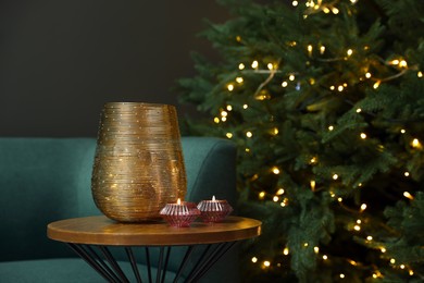 Photo of Vase, scented candles on table and beautiful Christmas tree with golden lights in living room