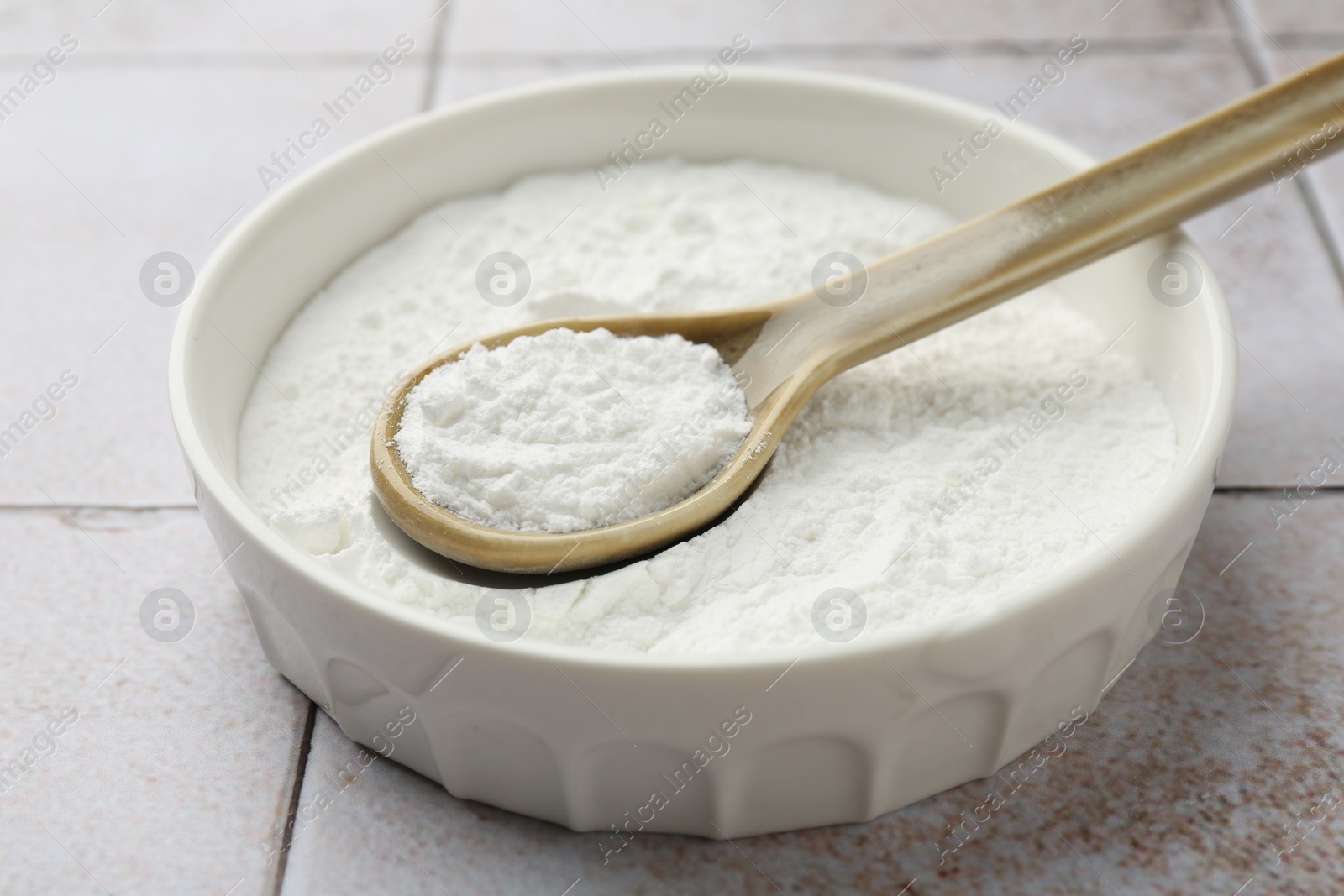 Photo of Baking powder in bowl and spoon on light tiled table, closeup