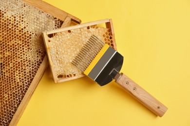 Photo of Hive frames with honeycombs and uncapping fork on yellow background, flat lay. Beekeeping