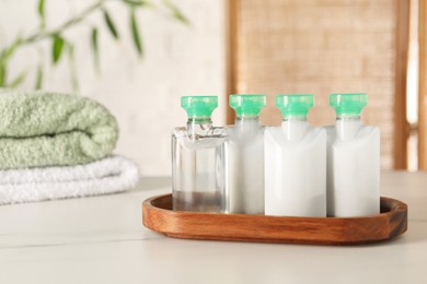 Mini bottles of cosmetic products on white table against blurred background. Space for text