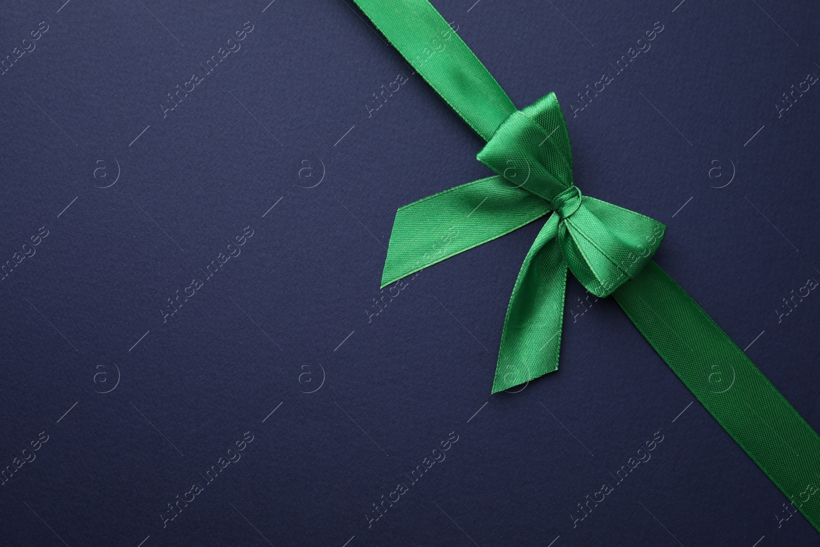 Photo of Green satin ribbon with bow on blue background, top view. Space for text