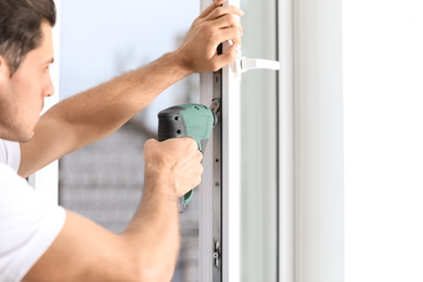 Photo of Construction worker repairing plastic window with screwdriver indoors, closeup