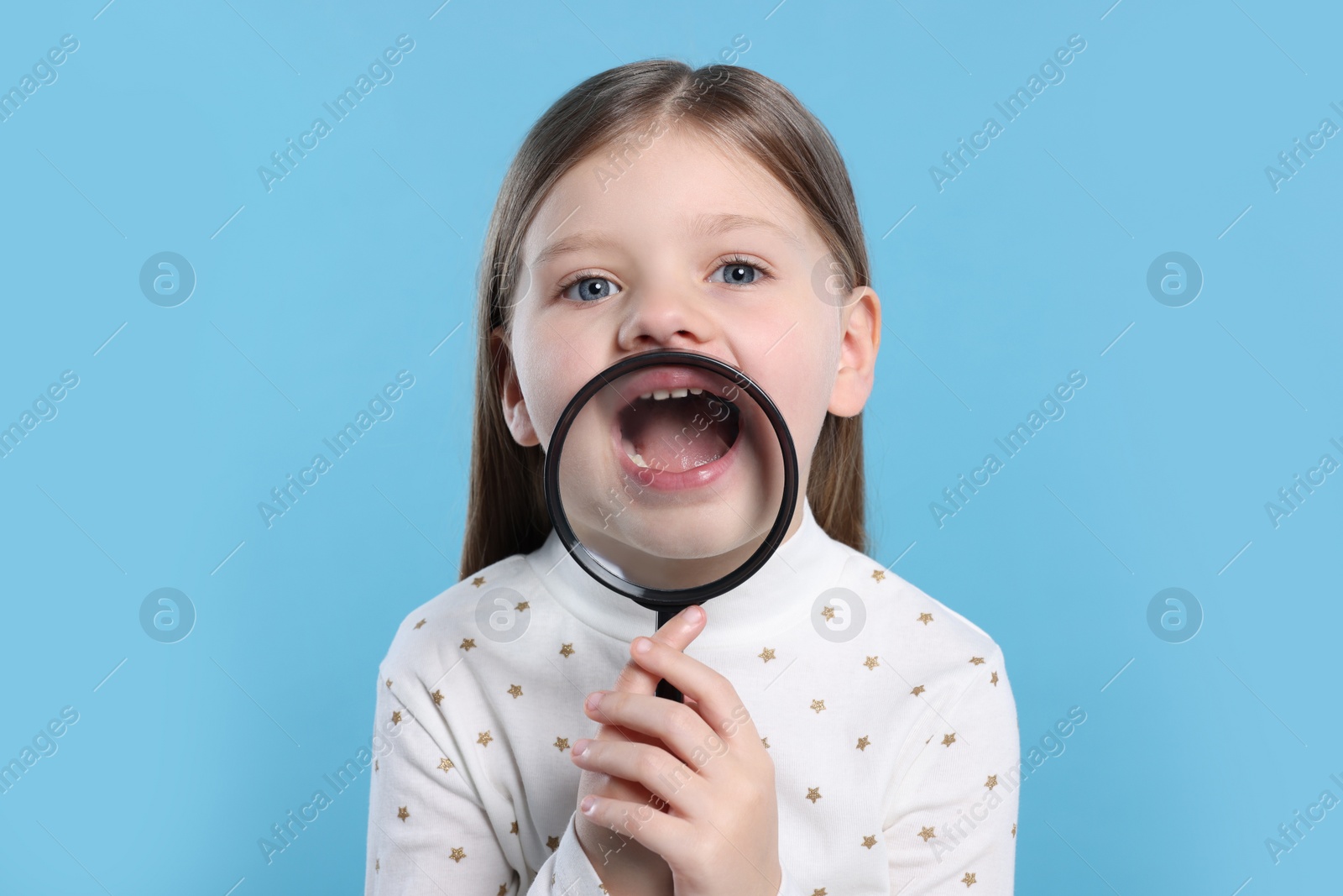 Photo of Cute little girl holding magnifier glass near her face on light blue background