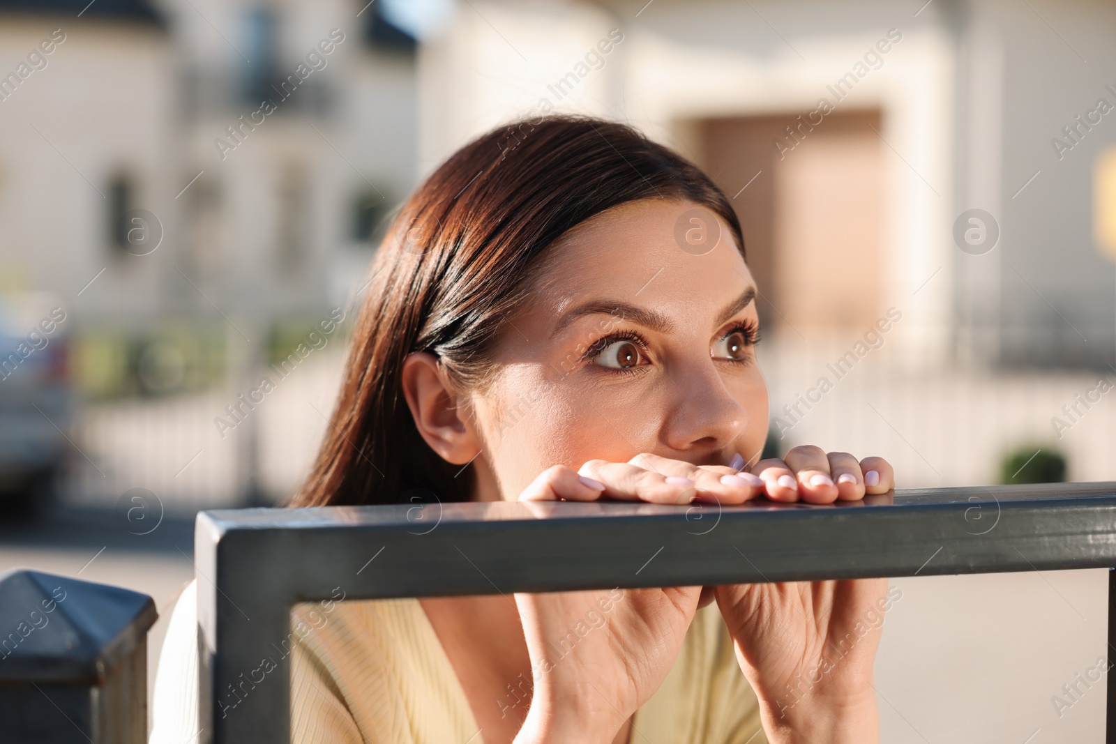 Photo of Concept of private life. Curious young woman spying on neighbours over fence outdoors