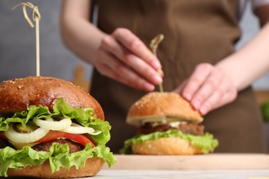 Photo of Woman making delicious vegetarian burger at white marble table, selective focus