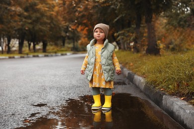 Photo of Cute little girl standing in puddle outdoors, space for text