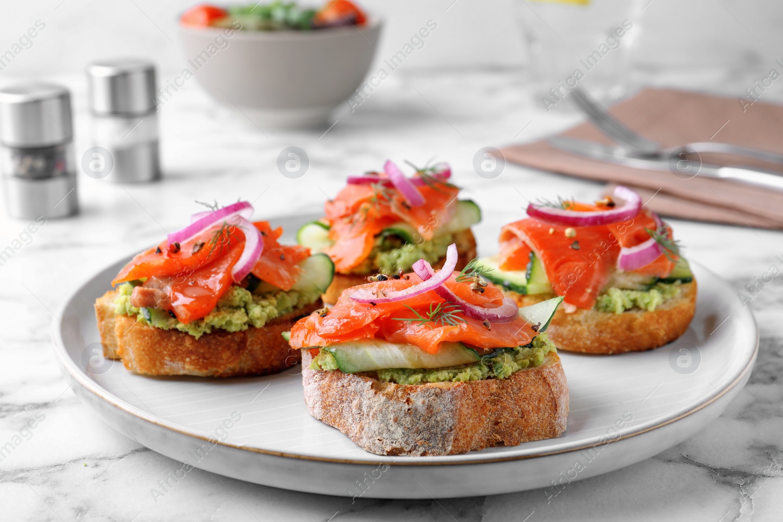 Photo of Delicious sandwiches with salmon, avocado, cucumber and onion on white marble table, closeup
