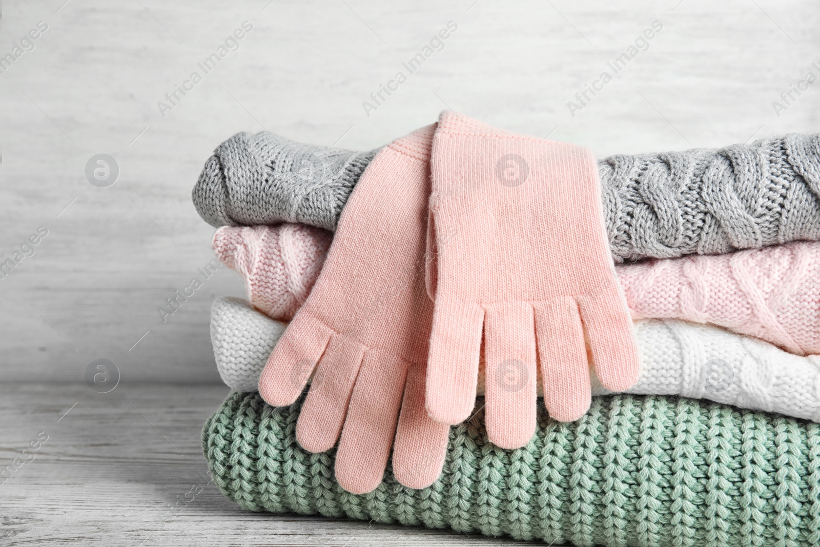 Photo of Stacked sweaters and gloves on wooden table, closeup. Autumn clothes