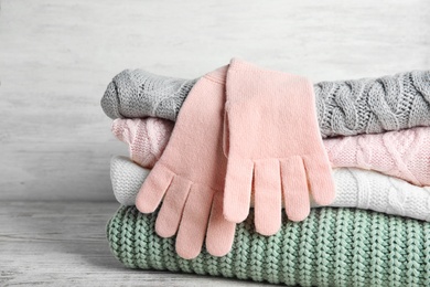 Photo of Stacked sweaters and gloves on wooden table, closeup. Autumn clothes