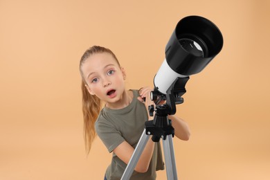 Surprised little girl with telescope on beige background