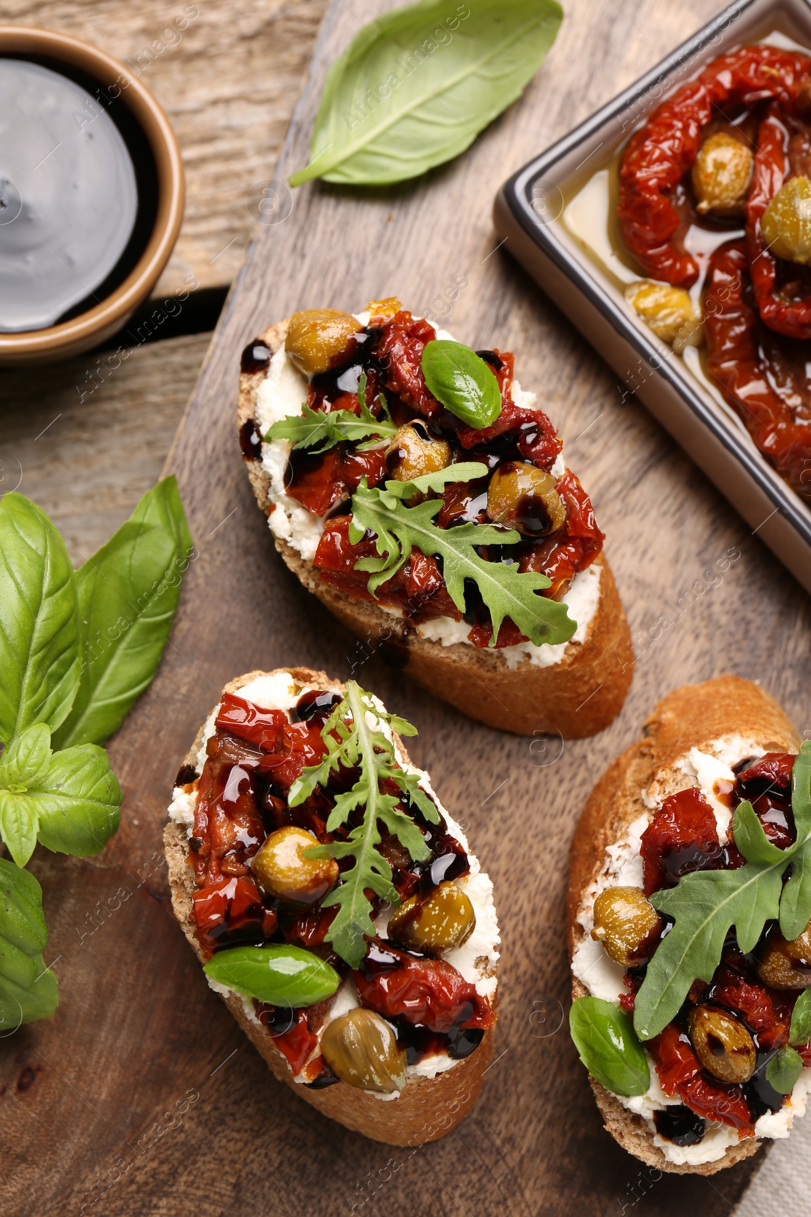 Photo of Delicious bruschettas with balsamic vinegar and toppings served on wooden table, flat lay