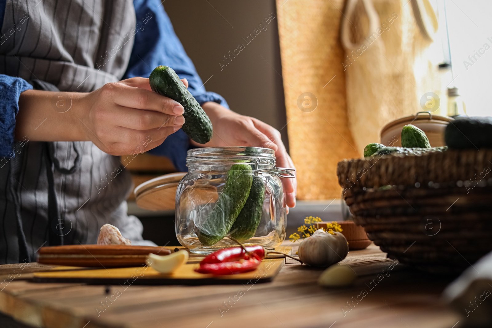 Photo of Woman putting cucumbers into jar at wooden table, closeup. Pickling vegetables