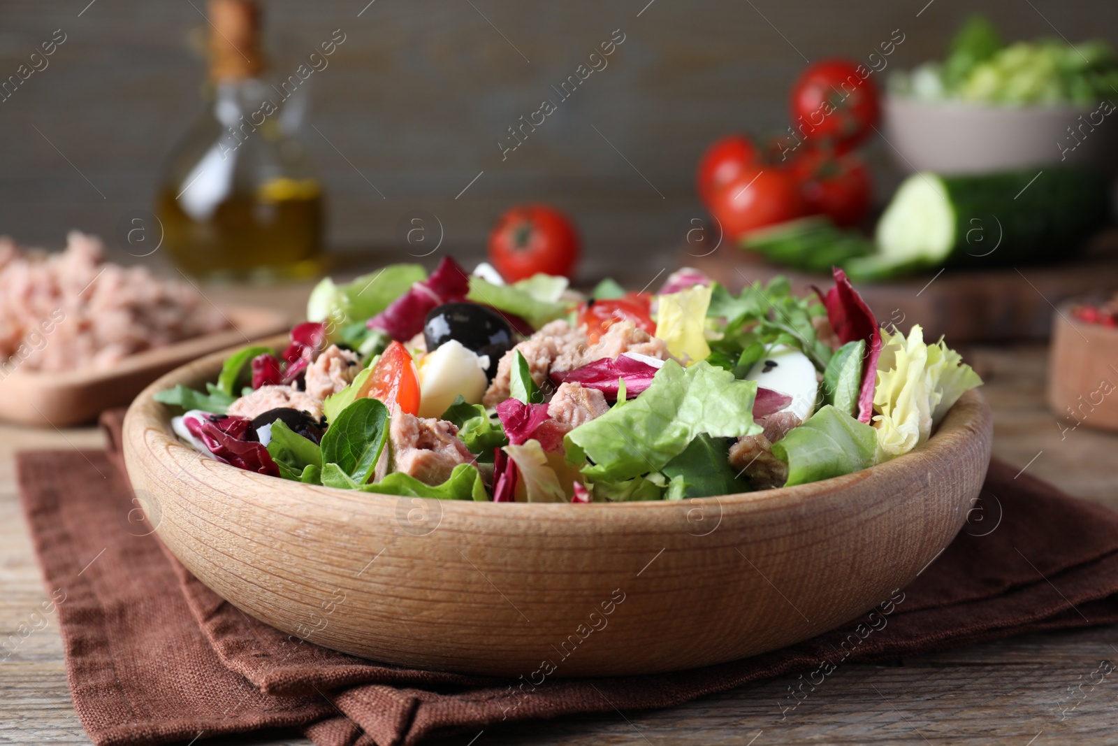 Photo of Bowl of delicious salad with canned tuna and vegetables on wooden table