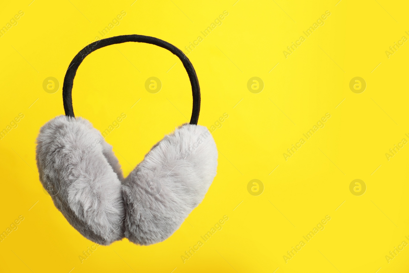 Photo of Stylish winter earmuffs on yellow background, space for text