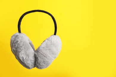Stylish winter earmuffs on yellow background, space for text