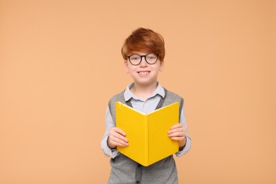 Smiling schoolboy with book on beige background