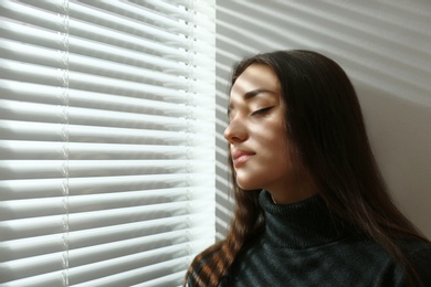 Photo of Young woman near window with Venetian blinds. Space for text