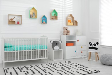 Photo of Comfortable crib near wall with color shelves in baby room. Interior design