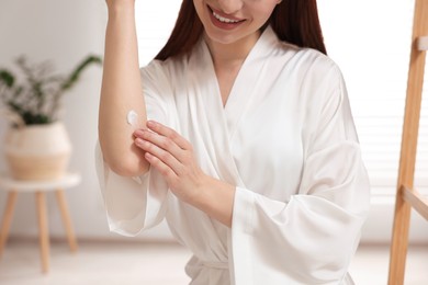 Young woman applying body cream onto elbow in bathroom, closeup