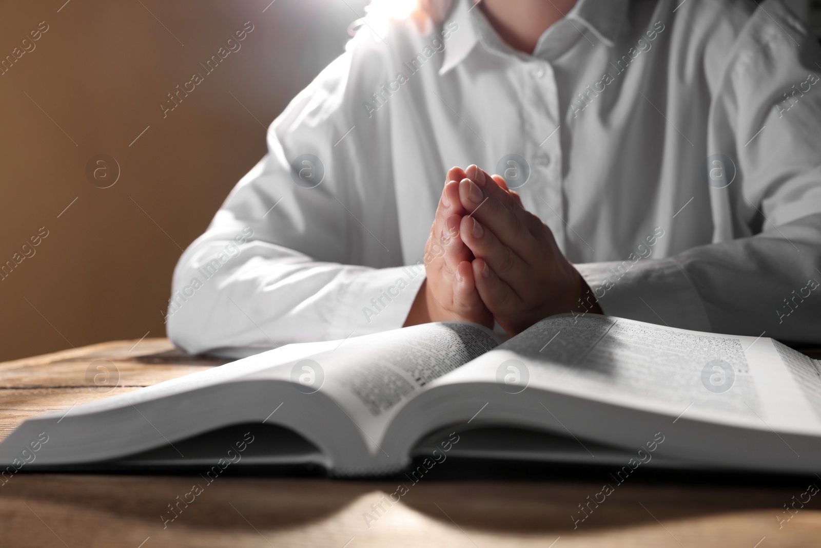 Photo of Woman holding hands clasped while praying over Bible at wooden table, closeup