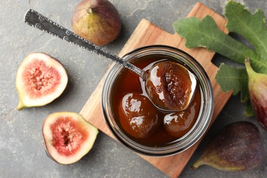 Photo of Jar of tasty sweet jam, fresh figs and green leaf on grey table, flat lay