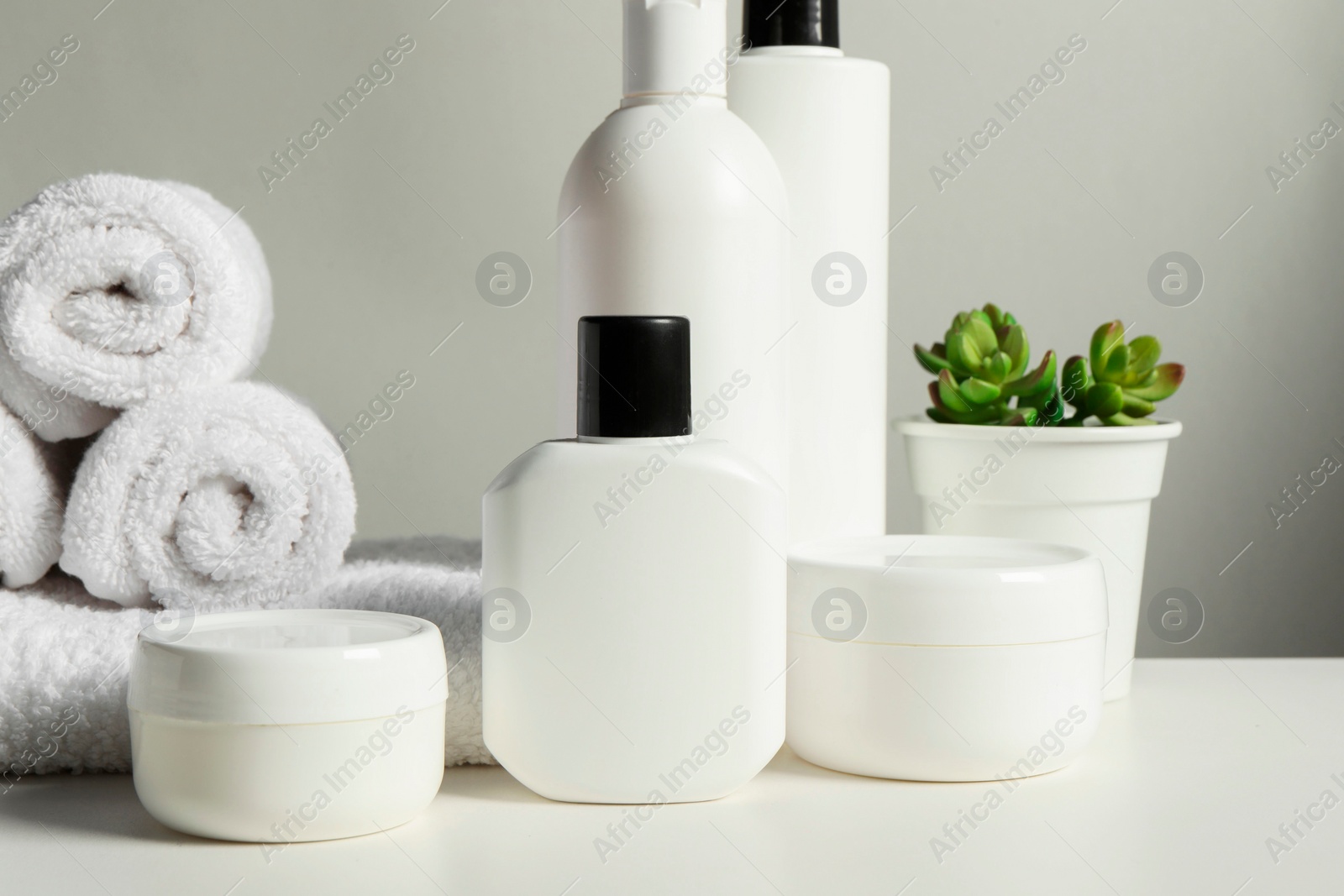 Photo of Different bath accessories, towels and houseplant on white table against grey background, closeup