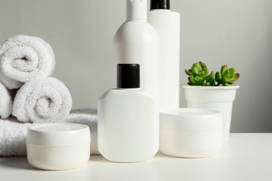 Different bath accessories, towels and houseplant on white table against grey background, closeup