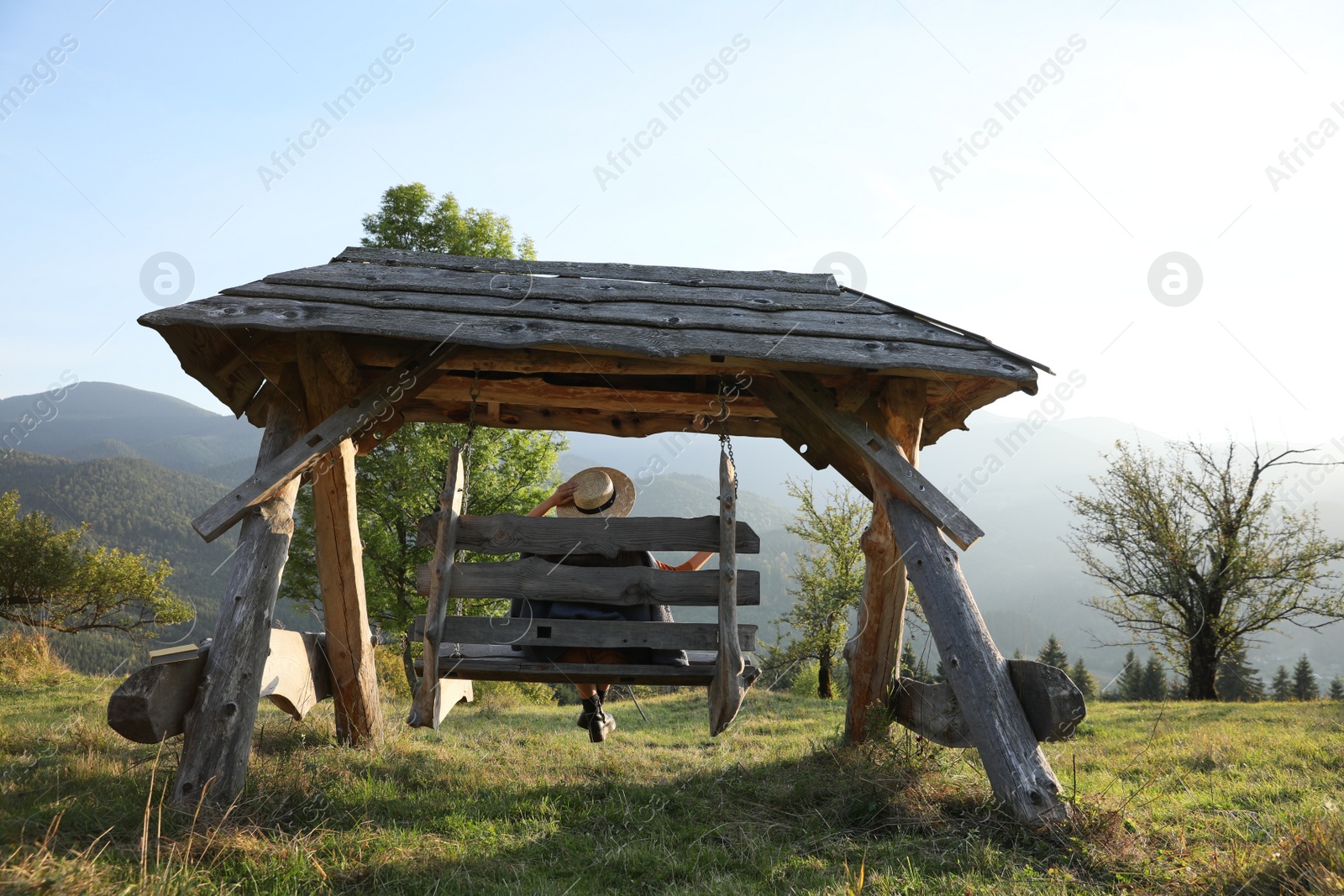 Photo of Young woman on wooden swing outdoors, back view