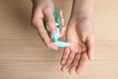 Photo of Woman applying antiseptic gel on hand against wooden background, top view