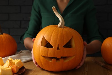 Photo of Woman with carved pumpkin at wooden table, closeup. Halloween celebration