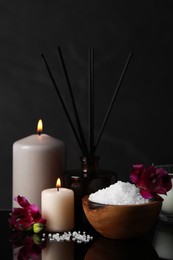 Photo of Beautiful spa composition with different care products and burning candles on mirror table against black background