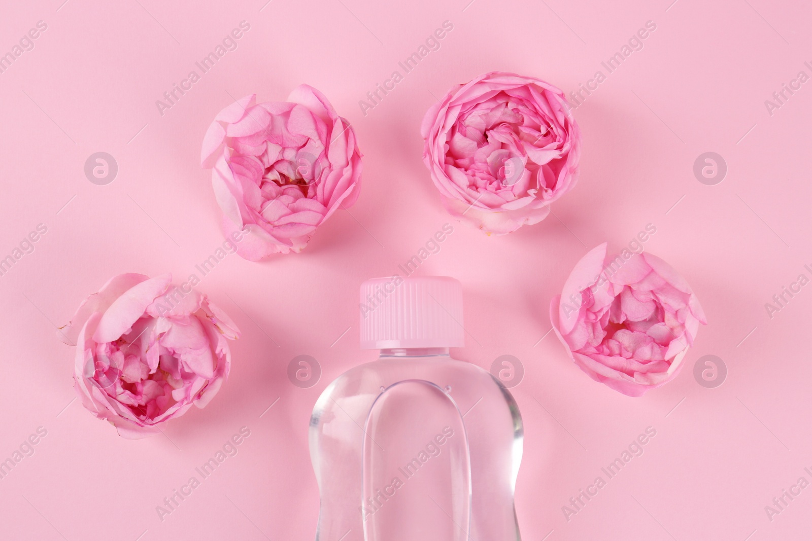 Photo of Bottle with baby oil and beautiful flowers on pink background, flat lay
