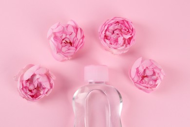 Photo of Bottle with baby oil and beautiful flowers on pink background, flat lay