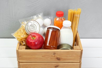 Photo of Humanitarian aid. Different food products for donation in crate on white wooden table, closeup