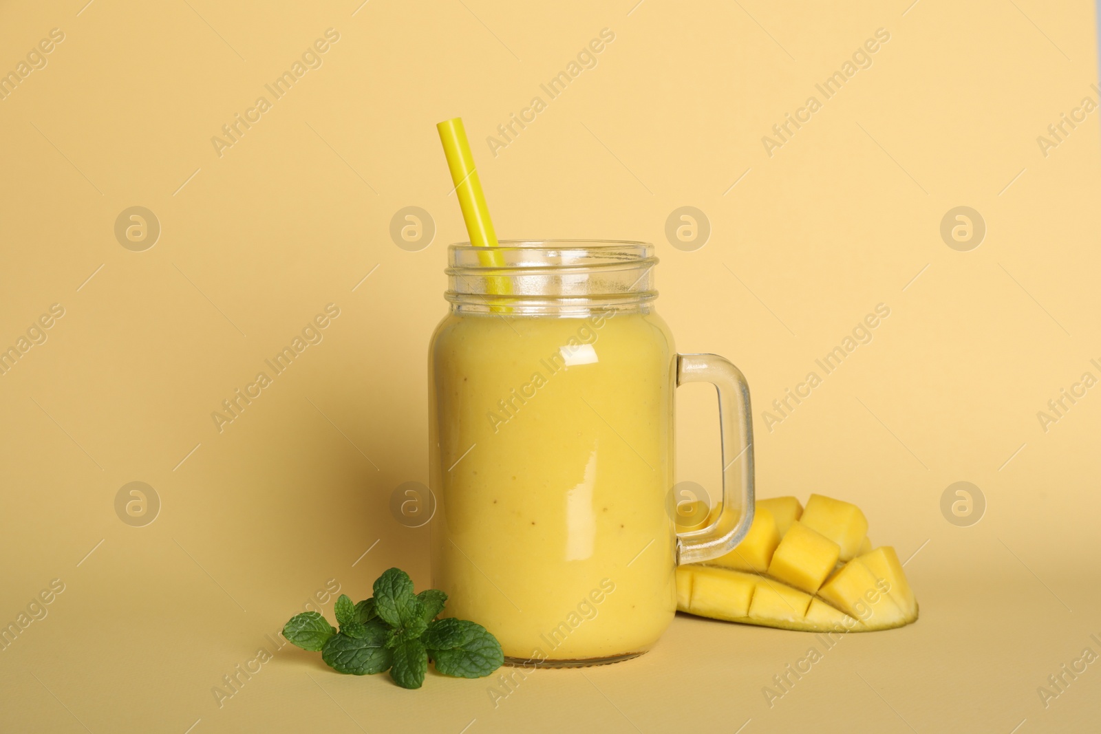 Photo of Mason jar of tasty smoothie with straw, mango and mint leaves on beige background