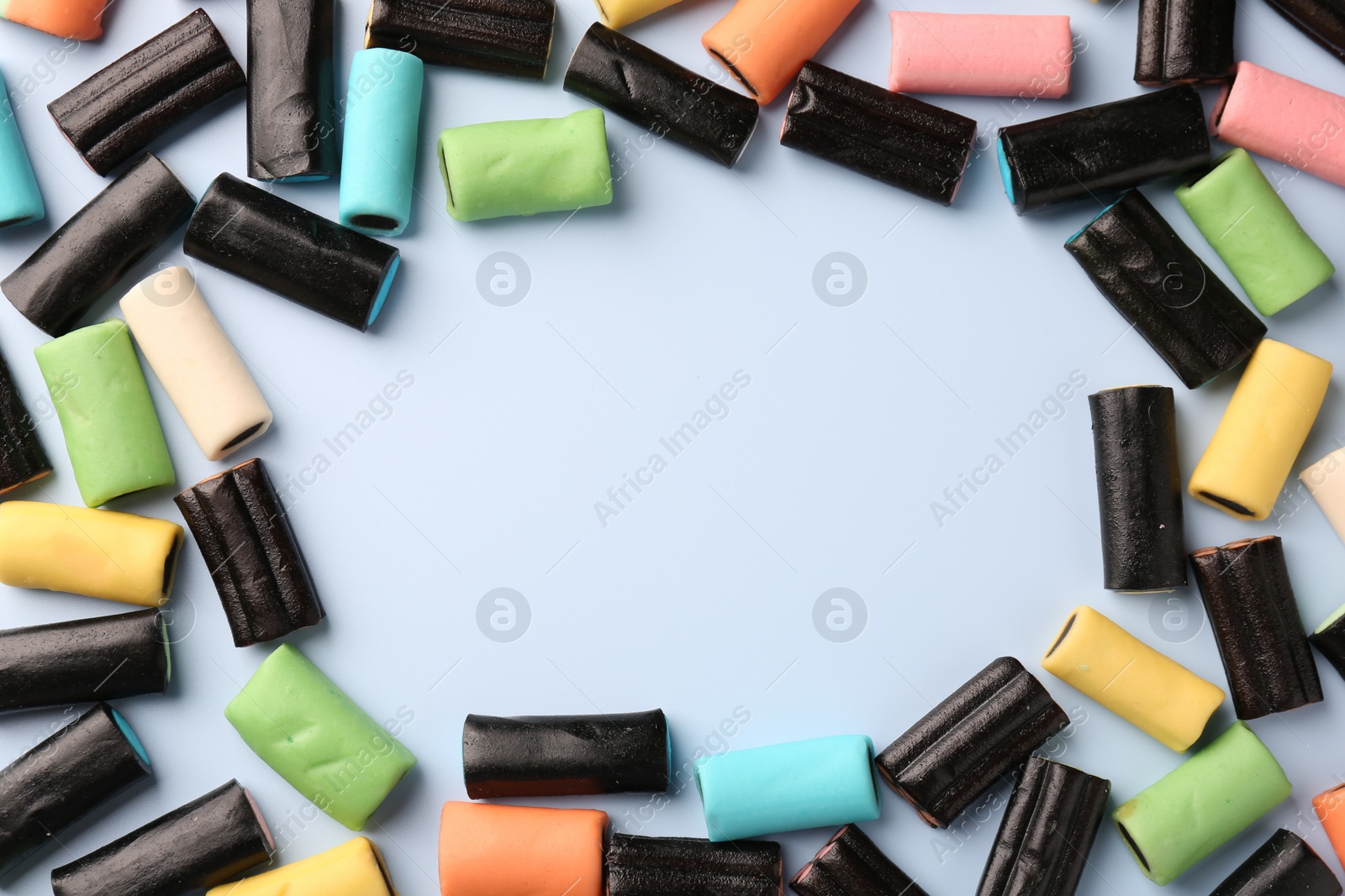 Photo of Frame made of tasty liquorice candies on light blue background, flat lay. Space for text