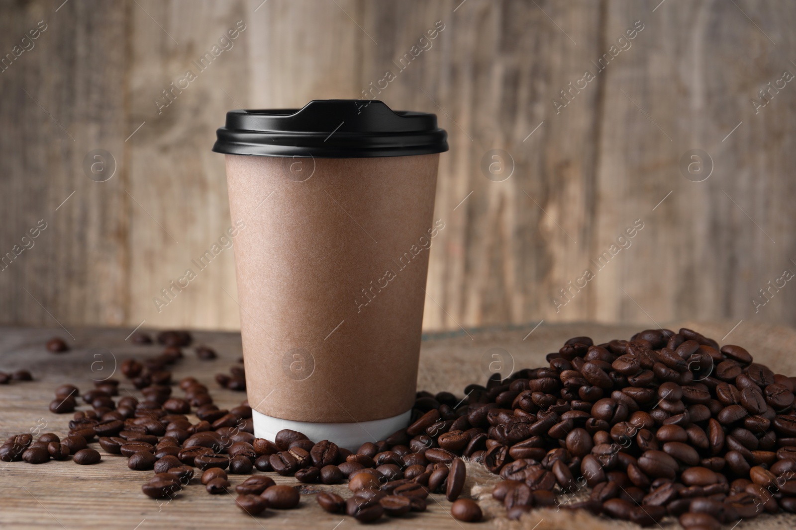 Photo of Coffee to go. Paper cup and roasted beans on wooden table, closeup