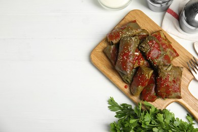 Delicious stuffed grape leaves with tomato sauce on white wooden table, flat lay. Space for text