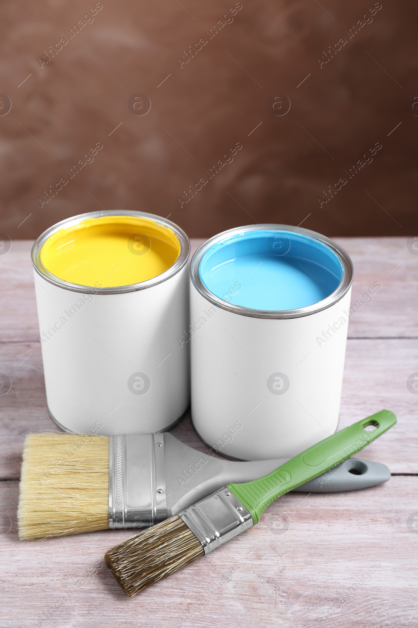 Photo of Cans of colorful paints and brushes on wooden table