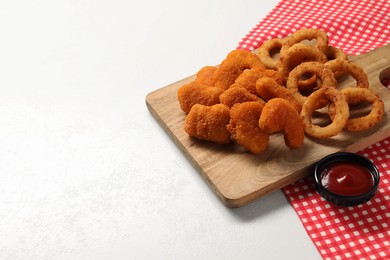 Tasty ketchup with chicken nuggets and onion rings on white textured table. Space for text