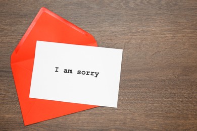 Apology. Card with phrase I Am Sorry and red envelope on wooden table, top view. Space for text