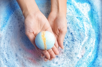 Photo of Woman holding color bath bomb over foam, top view