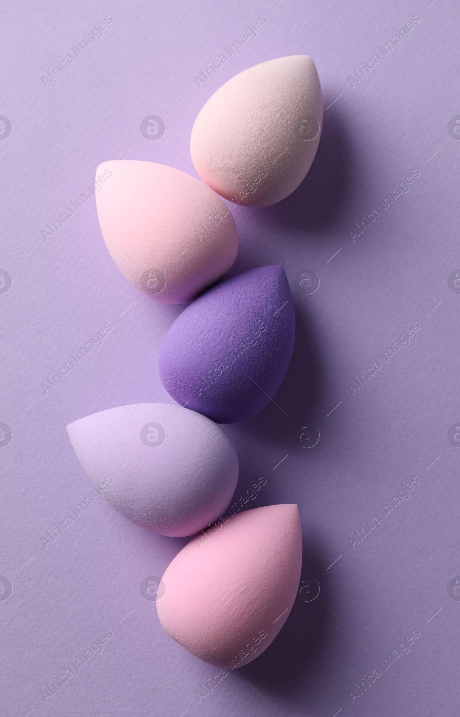 Photo of Many colorful makeup sponges on violet background, flat lay