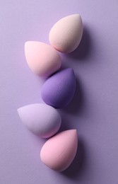 Many colorful makeup sponges on violet background, flat lay